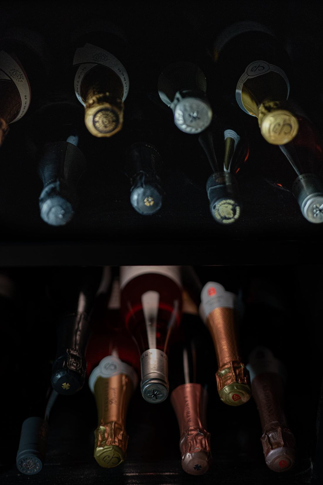 Bottles of wine, laid on their side, across 2 lit shelves.